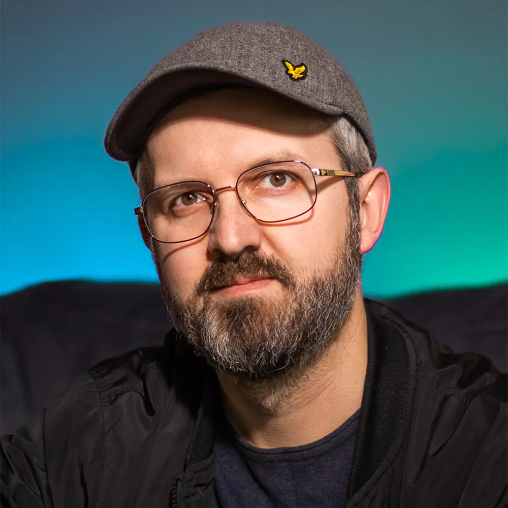 Portret brodatego mężczyzny w okularach i szarej czapce na niebiesko-zielonym tle